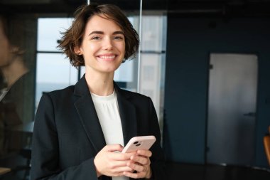 Şirkette çalışan satış elemanı portresi, cam duvarın yanında duran, cep telefonu tutan, gülümseyen, müşteriyi arayan, iş görüşmesi ayarlayan..