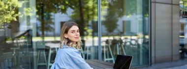 Dışarıda otururken dizüstü bilgisayar kullanan genç bir iş kadınının portresi. Kurumsal kadın görüntülü görüşme yapıyor..