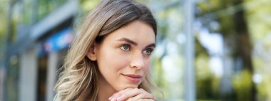 Genç bir kadının yakın portresi, umut dolu görünüyor ve gülümsüyor, elleri üzerinde uzanıyor, düşünüyor, dışarıda oturuyor..