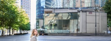 Bej takım elbiseli, şehir merkezinde yalnız oturan, ofis binasının yanında bekleyen iş kadınının dikey görüntüsü..