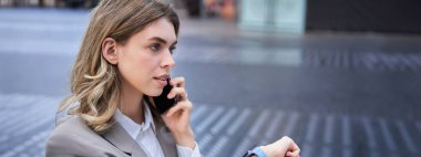 Meşgul bayan yönetici sokakta cep telefonuyla konuşuyor, toplantıya gidiyor, saati kontrol ediyor..