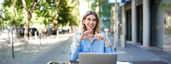 Portrait of beautiful corporate woman sitting with laptop outdoors, video chatting on laptop, talking happily, working outside office.