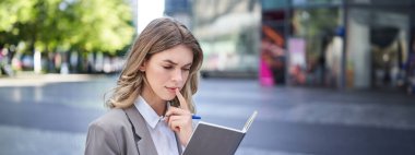 Kadın notlarını okurken konsantre oluyor, röportaj için hazırlanıyor. Takım elbiseli iş kadını deftere yazıyor, şehir merkezinde oturuyor..