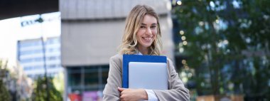 Genç bir kadının portresi, ofis müdürü dizüstü bilgisayarla ve iş dosyasıyla sokakta yürüyor, gülümsüyor..