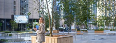 Güzel gülümseyen iş kadını iş molasında kahve içer, sokakta durur..