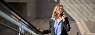 Yürüyen merdivende yürürken cep telefonuyla konuşan başarılı bir iş kadını..