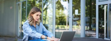 Başarılı bir iş kadını dışarıda çalışıyor, bilgisayarla, belgelerle ve belgelerle temiz havada oturuyor, bilgisayar ekranına bakıyor..