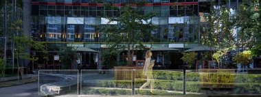 Bej takım elbiseli genç bir iş kadını silueti şehir merkezinde yürüyor, ofis binalarının yanında poz veriyor, işe gidiyor..