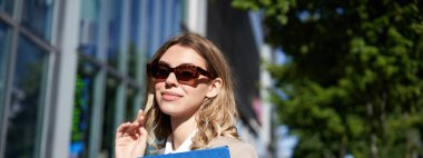 Güneş gözlüklü, takım elbiseli, iş belgeleriyle dolu bir klasörü olan, iş görüşmesine giden, dışarıda duran gülümseyen genç bir kadının yakın portresi..