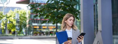 İş kadını kahve içiyor, elinde akıllı telefonuyla evrak tutuyor, ofiste çalışıyor, şehir merkezinde dışarıda duruyor..