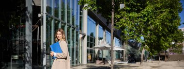 Bej takım elbiseli bir iş kadını portresi ve sokakta yürüyen yüksek topuklu ayakkabılar. Şirket kadını işe gidiyor, elinde belgelerle klasörü tutuyor..