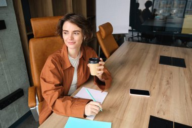 Ofiste çalışan genç bir kadın, konferans odasında kahve içiyor..