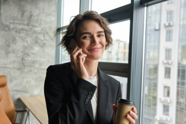 Ofiste kahvesini içen iş kadınının portresi, pencereden dışarı bakıp müşteriyle telefonda konuşmak, telefona cevap vermek..