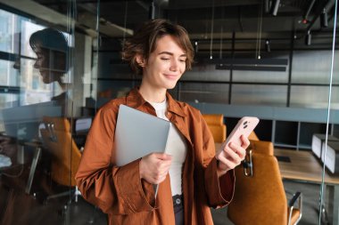 Ofiste çalışan, dijital göçebe portresi. Akıllı telefon kullanıyor, dizüstü bilgisayar tutuyor..