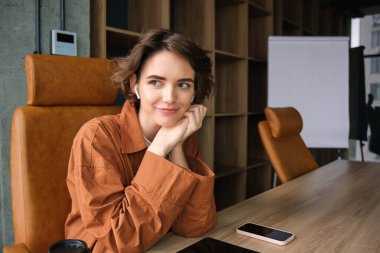 Genç bir ofis çalışanı, günlük giysiler içindeki bir çalışan masasında oturan ve gülümseyen bir iş kadını..