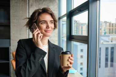 Bir kadın girişimcinin telefonuna cevap vermesi, ofiste durması, pencerenin dışına bakması, kahve içmesi, sohbet etmesi, takım elbise giymesi..