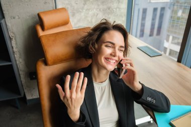 Cep telefonuyla konuşan kurumsal bir kadının portresi, ofisindeki bir telefona cevap vermek, gülmek, gülümsemek, sohbet etmek, sandalyesine yaslanmak..