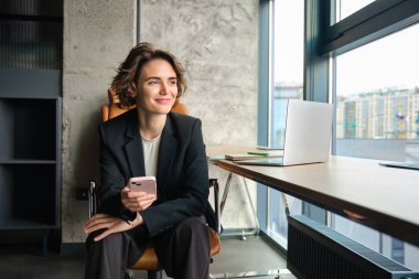 İş kadını ofisinde cep telefonuyla oturuyor..