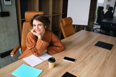 Ofisteki kadın girişimcinin portresi, konferans odasında belgelerle oturuyor, yazıyor, notlar alıyor ve çalışıyor..