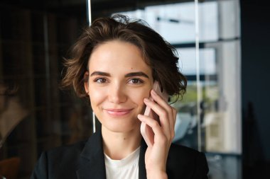 Başarılı bir iş kadınının portresi telefon görüşmesi yapıyor, ofiste duruyor ve müşteriyle konuşuyor..