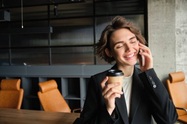 İş kadınının akıllı telefondan müşteriyi araması, telefona cevap vermesi konferans odasında durup kahve içmesi. Ofiste çalışan genç bayan girişimci..