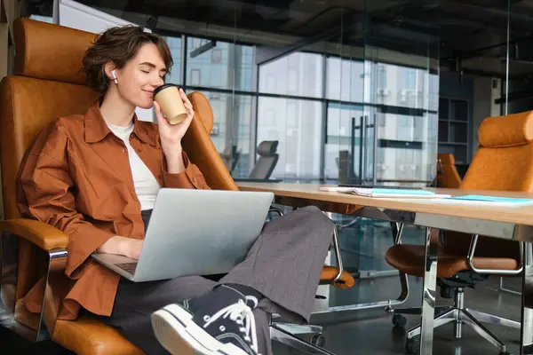 Portrait of young woman, programmer sits in office, works on laptop, uses computer, drinks coffee.