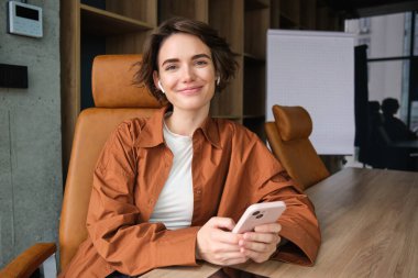 Genç bayan girişimcinin yakın portresi, günlük giysiler içinde satış elemanı, ofisinde oturuyor ve gülümsüyor..