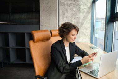 Ofisinde çalışan iş kadınının portresi, mesajlara cevap vermek için akıllı telefonu kullanıyor..