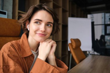 Genç bir ofis çalışanı, günlük giysiler içindeki bir çalışan masasında oturan ve gülümseyen bir iş kadını..