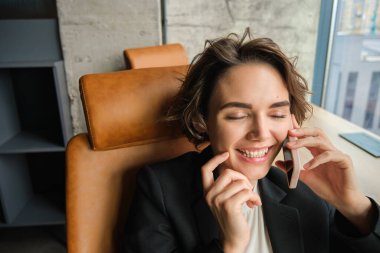 Cep telefonuyla konuşan kurumsal bir kadının portresi, ofisindeki bir telefona cevap vermek, gülmek, gülümsemek, sohbet etmek, sandalyesine yaslanmak..