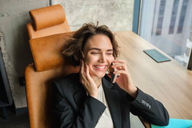 Cep telefonuyla konuşan kurumsal bir kadının portresi, ofisindeki bir telefona cevap vermek, gülmek, gülümsemek, sohbet etmek, sandalyesine yaslanmak..