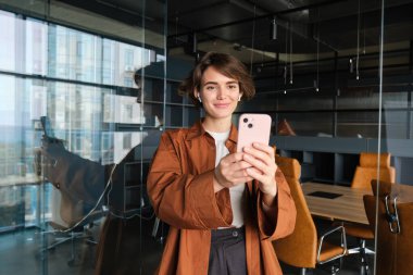 Genç kadın portresi, içerik yaratıcısı, ofisteki Sm yöneticisi, akıllı telefonlu bir video yaratıyor, cep telefonuyla poz veriyor.