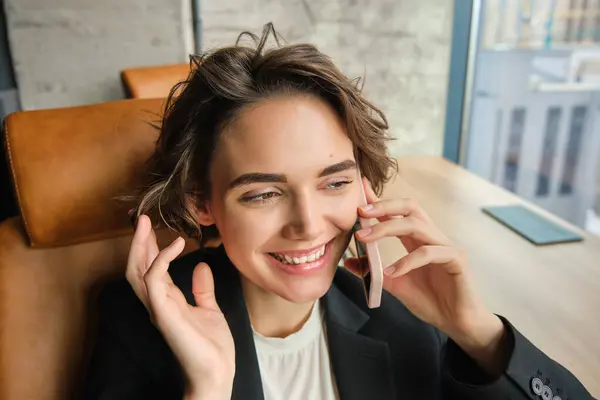 Image of successful woman talking on mobile phone, having a conversation over the telephone, answering client, sitting and working in an office.