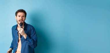 Kameraya bakan tutkulu şarkıcı, mikrofonda şarkı söyleyen, mavi arka planda karaoke yapan. Boşluğu kopyala