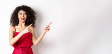 Şaşırmış, kıvırcık saçlı, makyajlı, kırmızı elbiseli, şaşkın ve mutlu görünen bir kadın..
