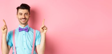 Neşeli yakışıklı adam kameraya gülümsüyor, parmaklarını havaya kaldırıyor, pembe arka planda reklam yapıyor..