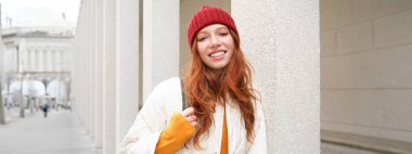 Female tourist in red hat with backpack, sightseeing, explores historical landmarks on her trip around europe, smiling and posing on street.
