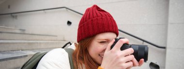 Urban people and lifestyle. Happy redhead woman takes photos, holding professional digital camera, photographing on streets.