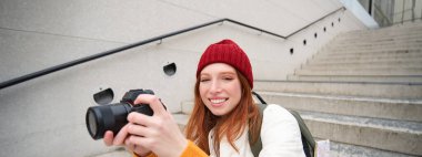 Portrait of female photographer walking around city with professional camera, taking pictures capturing urban shots, photographing outdoors.