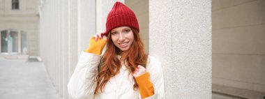 Female tourist in red hat with backpack, sightseeing, explores historical landmarks on her trip around europe, smiling and posing on street.