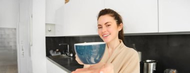 Çekici, gülümseyen bir kadının portresi. Sana fincanı veriyor, sabah kahvesini ikram ediyor ve mutlu görünüyor. Bornozla mutfakta duruyor..