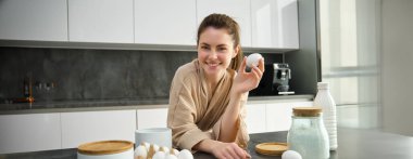 Çekici, genç, neşeli kız mutfakta yemek pişiriyor, para kazanıyor, yemek tarifi kitabını tutuyor, fikirleri var..