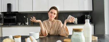 Çekici, genç, neşeli kız mutfakta yemek pişiriyor, para kazanıyor, yemek tarifi kitabını tutuyor, fikirleri var..