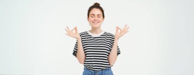 Genç bir kadının portresi dinleniyor, zen hissediyor, meditasyon yapıyor, mutlu bir şekilde gülümsüyor, sakin bir yüz ifadesi, beyaz arka planda duruyor..