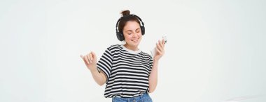 Akıllı telefon dansı yapan, kablosuz kulaklıkla müzik dinleyen, favori şarkıların tadını çıkarmak için cep telefonu uygulaması kullanan, beyaz arka planda izole edilmiş bir kız..
