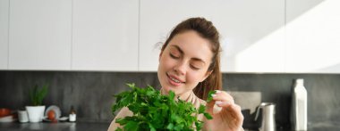 Bir buket maydanozla gülümseyen güzel bir kızın portresi, mutfakta durup yemek pişirmek, sağlıklı taze salata ya da yemeğe şifalı otlar eklemek,.