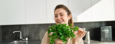 Bir buket maydanozla gülümseyen güzel bir kızın portresi, mutfakta durup yemek pişirmek, sağlıklı taze salata ya da yemeğe şifalı otlar eklemek,.