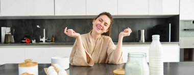 Çekici, genç, neşeli kız mutfakta yemek pişiriyor, para kazanıyor, yemek tarifi kitabını tutuyor, fikirleri var..
