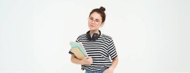 Eğitim konsepti. Gülümseyen esmer kız, günlük giysiler içinde öğrenci, kitaplarını tutuyor, ders çalışıyor, kulaklık takıyor, kendinden emin ve mutlu görünüyor, beyaz arka planda izole edilmiş..