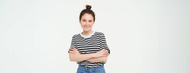 Çekici, şık bir genç kadın portresi, 25 yaşında, tişört giyiyor, kollarını göğsüne dayamış, gülümsüyor, kendinden emin, beyaz arka planda soyutlanmış..